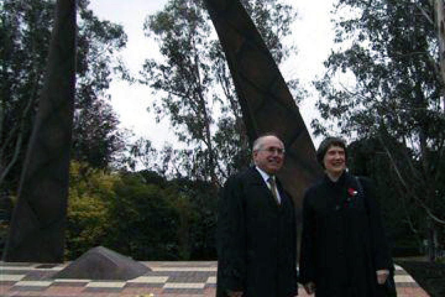 Two people in black coats standing together in front of handle shaped bronze memorial
