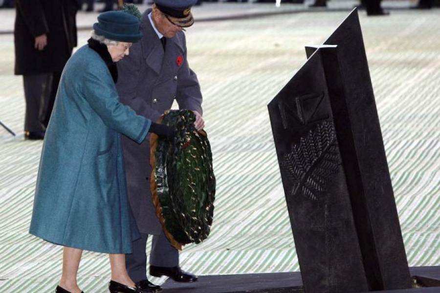 A woman and a man in blue military uniform about to place a floral wreath on the ground