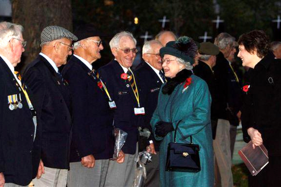 Two smiling women talking to a line of elderly men wearing medals