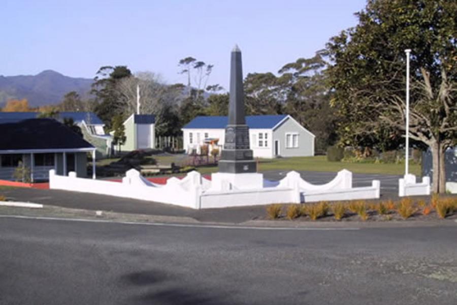 Stone obelisk with trees and wooden house in the background