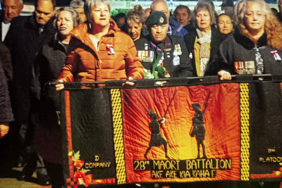 Group of people, some wearing war medals, carrying banner with the words '28th Maori Battalion Ake Ake Kia Kaha.