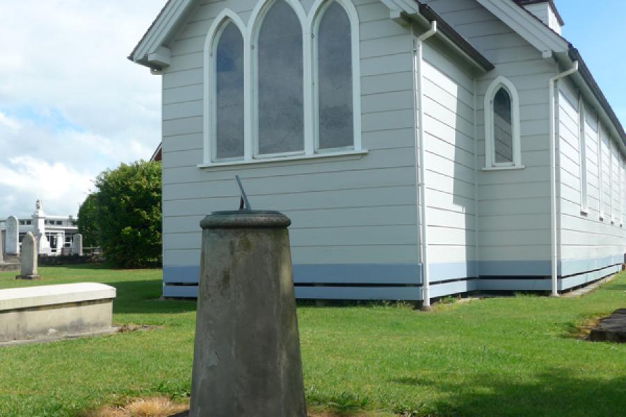 Sundial on concrete plinth in front of wooden church building