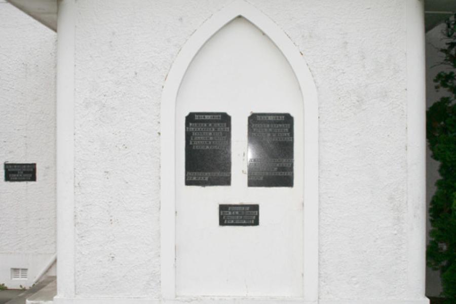 View of the entrance of the church. On the wall are two black plaques below an inscription in red letters that reads: 'Waimumu Memorial Church