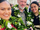 Two women each side of man wearing lei and smiling at camera