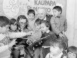Children gathered around with two men and a book at a Kohanga Reo