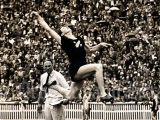 Woman in black sports uniform jumping through the air with huge crowd watching in the backgound 