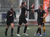 Three girls dressed in black football uniforms, playing football in the rain, high-five each other.