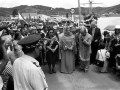 Group of Māori men and women carrying flags on road next to sea