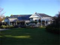 View of single-story house surrounded by trees, shrubs and grass lawn