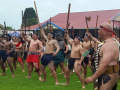 Group of bare-chested Māori men and boys carrying taiaha staffs with arms raised