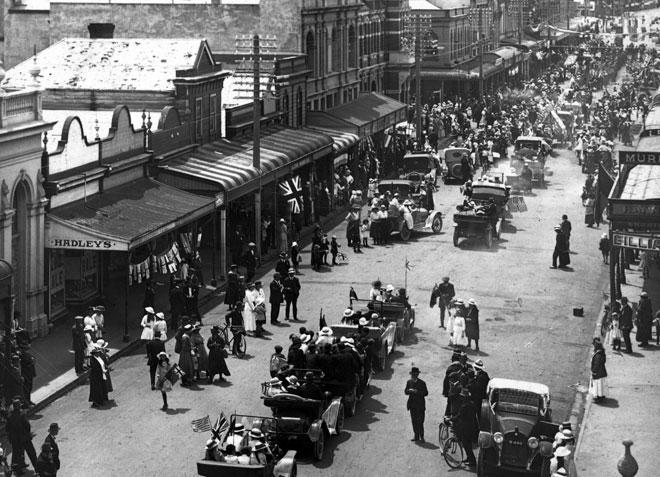Busy street with cars and people gathered on road with buildings on either side