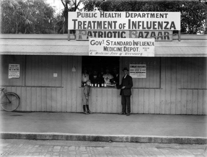 Two people standing outside building with a sign Government Standard Influenza Medicine