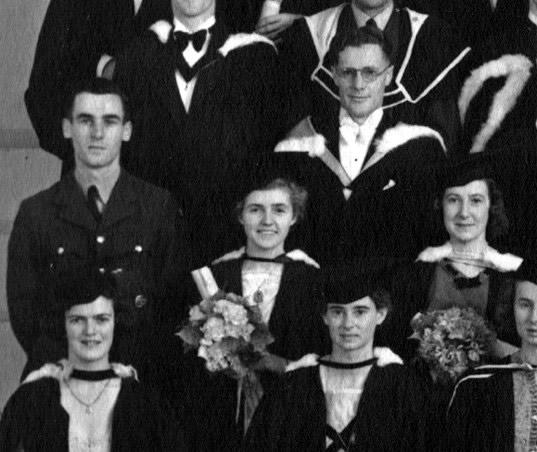 Group of graduates  - two holding flowers - and man in a soldier's uniform