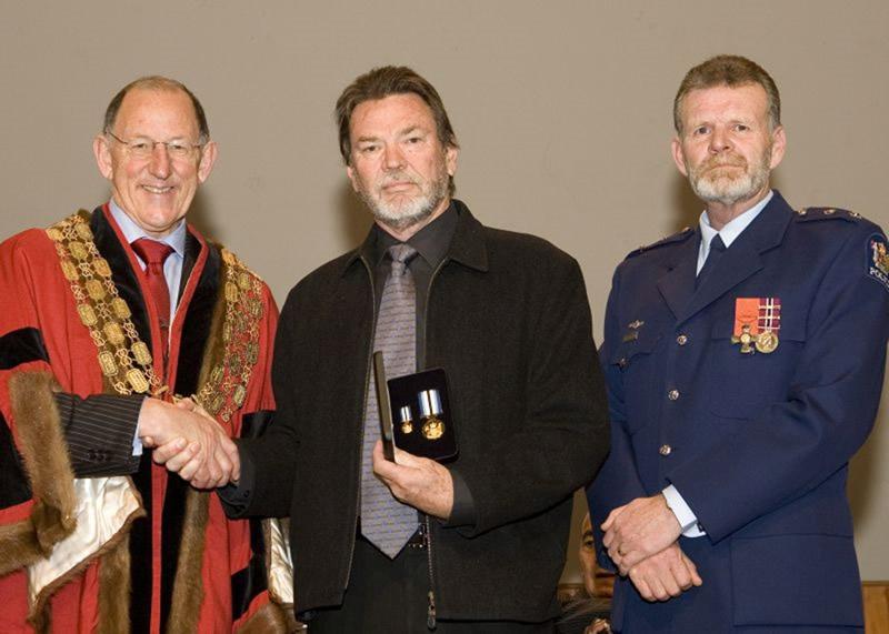 The Mayor of Auckland and a police officer either side of Ian Hambly holding his medals