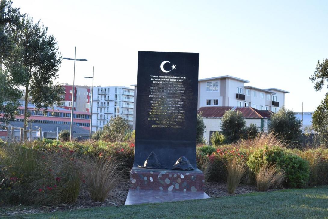 Bronze plaque above reddish-brown polished concrete plinth featuring the shapes of two military hats