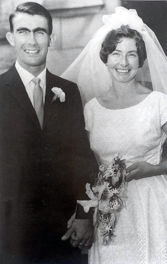 A man in a suit and woman in wedding gown posing in front of building