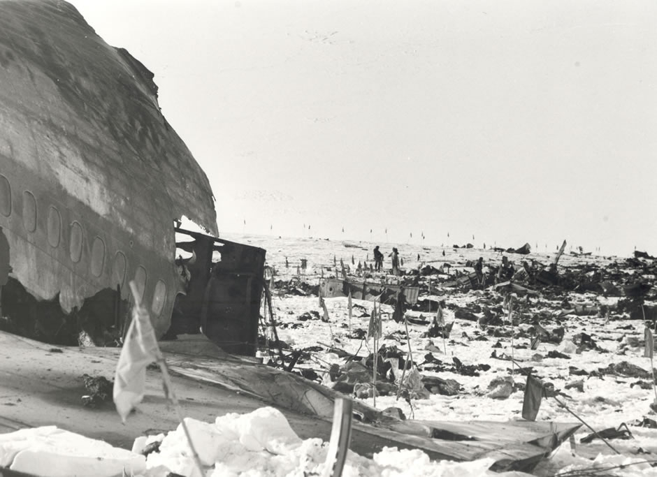Wreckage of part of airplane fuselage with debris scattered over ice. Flags dot the landscape