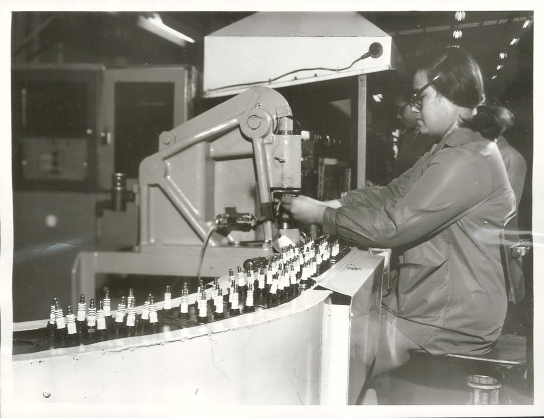 Seated woman working on a spark plug assembly line 