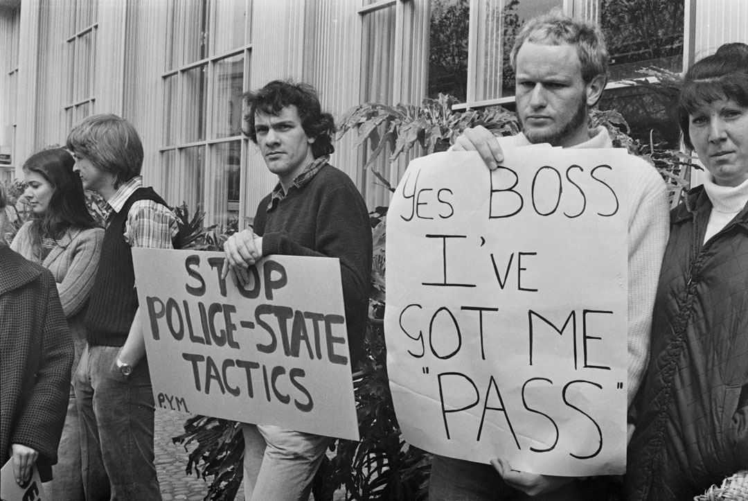 Protestors holding signs 'Stop state tactics' and 'Yes boss, I've got me pass'