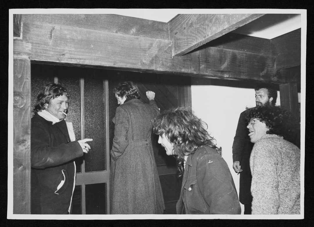 Group of five men laughing as one knocks on a door