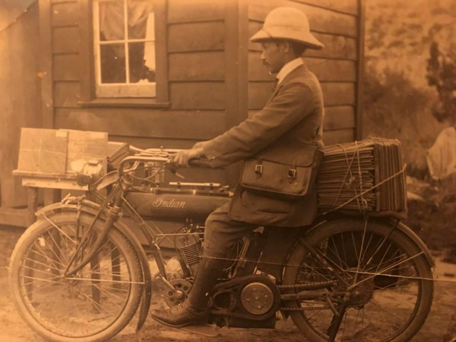 Cromwell Shepherd sitting on a motorbike outside of a house.