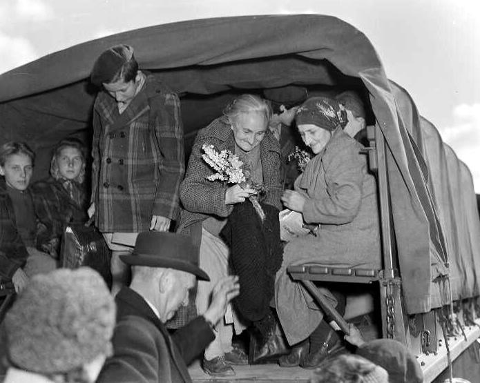 Girls and women crowded into the back of a canvas-covered truck. An older woman holds a bunch of flowers.
