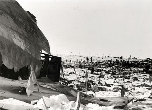 Debris from aircraft strewn over snow with flags planted amongst them.